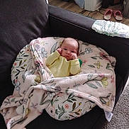 Kinsley joined the competition — help win amazing prizes! baby, blanket, couch, floral_pattern, indoors, infant, person, cozy, furniture, carpet, floor, slippers, plant, home, relaxing, yellow_clothing, cute, wrapped, resting, soft