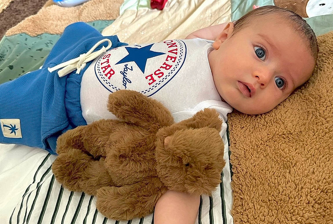 Milo participe au concours pour gagner de l'argent avec cette photo : baby, bed, blanket, blue_eyes, child, clothing, comfort, converse, cute, indoor, infant, laying_down, plush_toy, portrait, sleepwear, soft_texture, striped_sheet, teddy_bear, toy, young_child