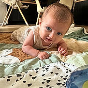 Milo a rejoint le concours — aidez-le/la à gagner de superbes lots ! baby, infant, blue_eyes, quilt, blanket, indoor, floor, high_chair, dining_table, chair, wood_floor, curious, person, face, child, crawling, home, furniture, playful, clothing