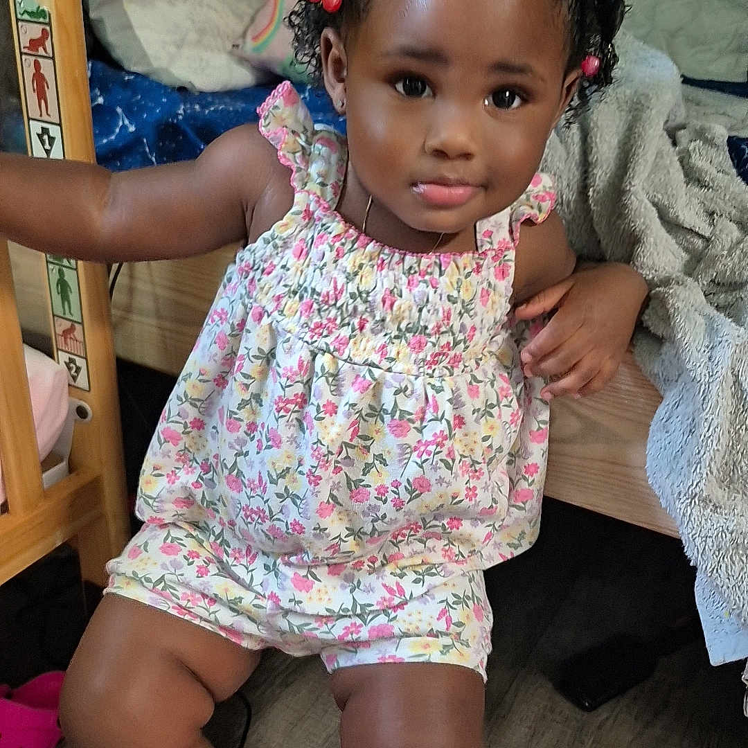 Monai joined the competition — help win amazing prizes! baby, bedroom, blanket, child, clothing, cute, expression, floor, floral_clothing, furniture, hair_beads, indoor, person, pigtails, pink_socks, plush_toy, skin, smiling, toddler, wooden_furniture
