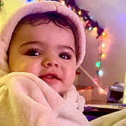 Lilith is registered to the contest to win money with this photo: baby, child, closeup, colorful_lights, cozy, cute, decor, eyes, face, happy, holiday_lights, hoodie, indoor, infant, person, pink_clothing, portrait, smiling, soft_texture, warm