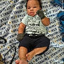 baby, infant, blanket, blue_clothing, mittens, shorts, lying_down, face, cute, child, text_on_clothing, pattern, floor, indoor, skin, foot, hand, expression, portrait, soft_texture