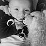 baby, infant, stuffed_animal, plush_toy, cuddle, blanket, face, eyes, hand, cozy, monochrome, black_and_white, soft_texture, portrait, child, smiling, cute, indoor, comfort, young
