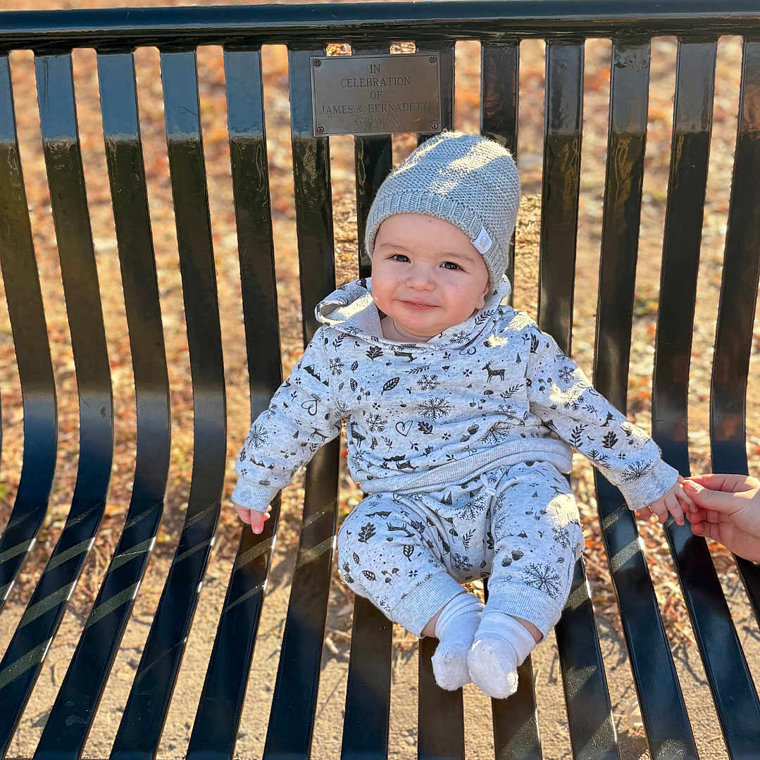 Ayden joined the competition — help win amazing prizes! baby, child, infant, sitting, bench, park, outdoor, autumn, leaves, sunlight, knit_hat, winter_clothing, onesie, socks, smiling, portrait, face, hand, family, playground