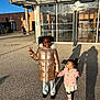 boots, building, child, children, coat, curly_hair, glass, happy, holding_hands, jacket, outdoor, pavement, peace_sign, pigtails, playful, reflection, shadow, smile, sunlight, toddler