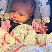 Sophia is registered to the contest to win money with this photo: baby, infant, blanket, car_seat, child, face, hand, clothing, pink, soft, cozy, cute, person, newborn, portrait, seatbelt, indoor, expression, wrapped, babywearing