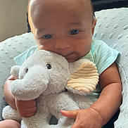 Kruz is registered to the contest to win money with this photo: baby, infant, child, plush_toy, elephant, hugging, sitting, portrait, smiling, face, eyes, hands, short_hair, striped_clothing, mint_green, soft_blanket, bed, indoor, window_blinds, cozy