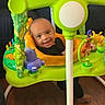 Kruz is registered to the contest to win money with this photo: baby, child, infant, smiling, happy, portrait, playtime, activity_center, baby_jumper, toys, colorful, green, indoor, living_room, couch, wood_floor, seated, face, family, playful