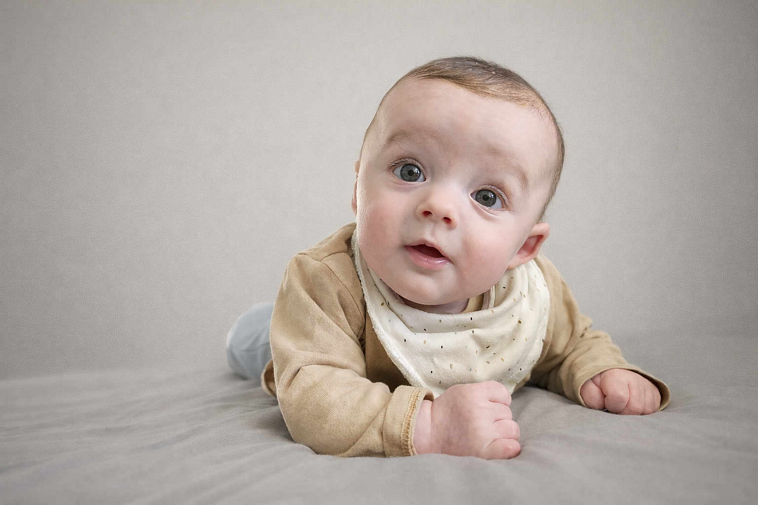 Elio participe au concours pour gagner de l'argent avec cette photo : baby, infant, child, tummy, face, eyes, expression, clothing, beige, blanket, soft_background, portrait, cute, indoors, head_tilt, skin, hands, laying_down, gaze, curious
