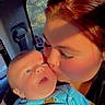 River is registered to the contest to win money with this photo: baby, woman, kiss, car_interior, blue_clothing, sports_pattern, window, seatbelt, affection, closeup, child, person, sunlight, face, parent, love, transport, casual, indoor, portrait