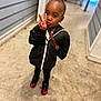 child, peace_sign, black_jacket, red_bow, sneakers, standing, alleyway, concrete_floor, earrings, shoulder_bag, person, fashion, cute, outdoor, portrait, young_child, expression, casual_wear, urban, playful