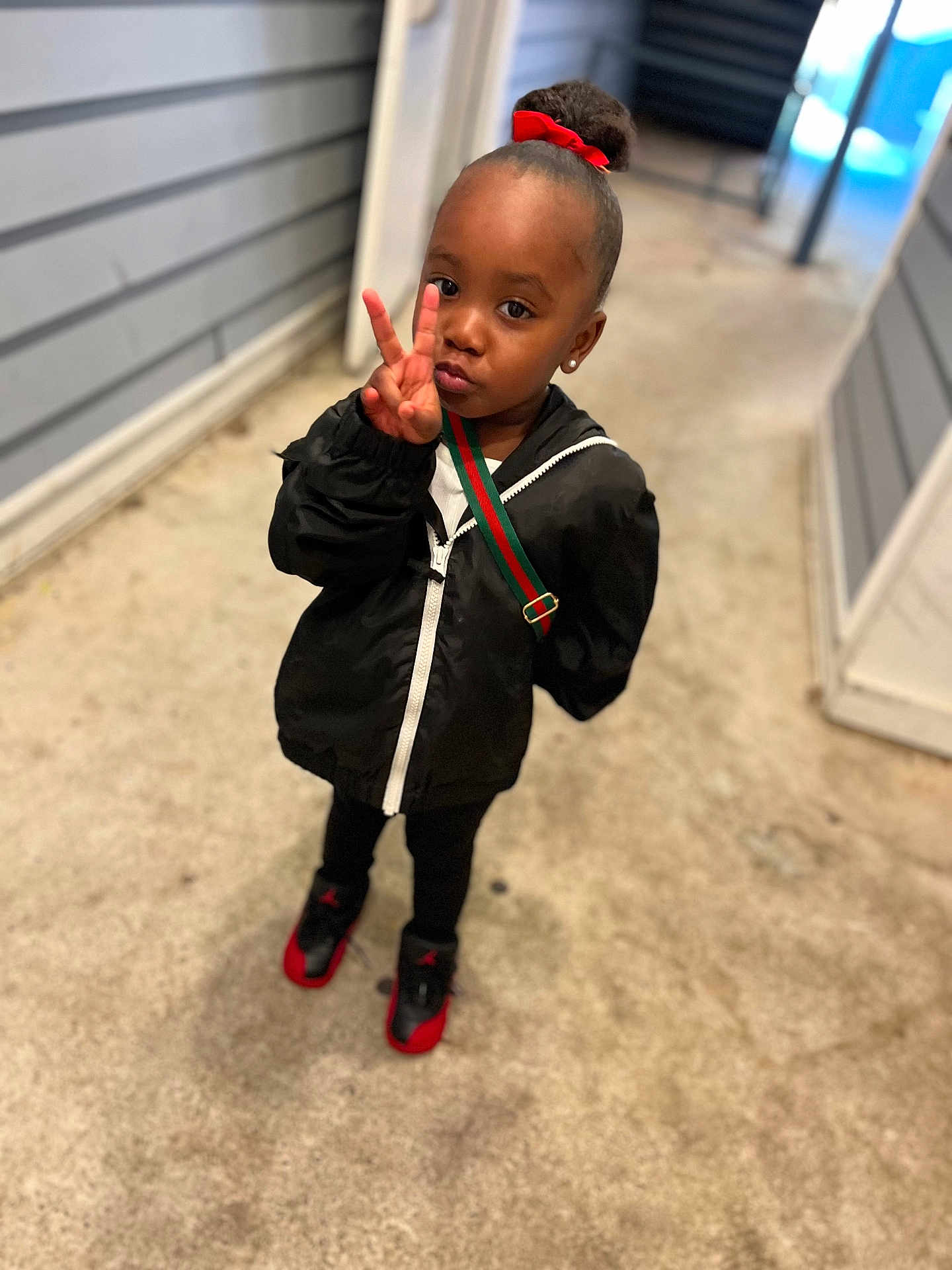 Kelani joined the competition — help win amazing prizes! child, peace_sign, black_jacket, red_bow, sneakers, standing, alleyway, concrete_floor, earrings, shoulder_bag, person, fashion, cute, outdoor, portrait, young_child, expression, casual_wear, urban, playful