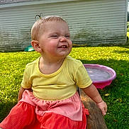 Gabriella Trout is registered to the contest to win money with this photo: toddler, child, outdoor, grass, bench, yellow_shirt, coral_shorts, pink_pool, shed, smiling, happy, playful, sunlight, grass_lawn, wood, person, cute, expression, summer, daytime