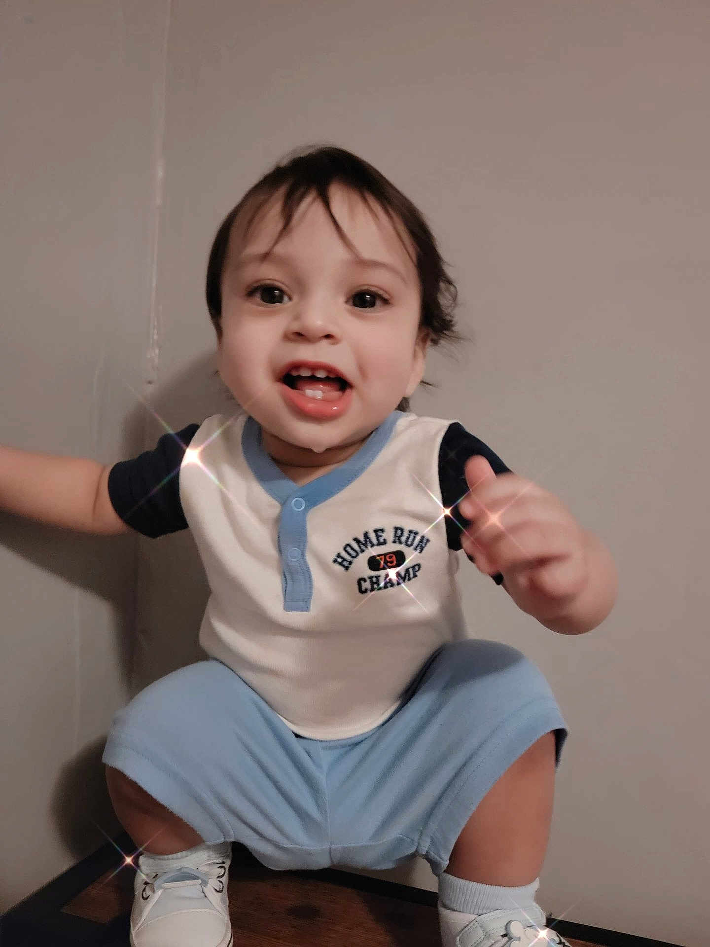 Elias is registered to the contest to win money with this photo: toddler, child, happy, smiling, squatting, blue_clothing, white_shoes, shorts, short_sleeve_shirt, indoor, person, cute, playful, young_child, face, hair, light_skin, casual, footwear, expression