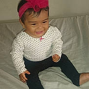 Skyler joined the competition — help win amazing prizes! baby, child, smiling, sitting, headband, pink, flower, polka_dot, long_sleeve, pants, barefoot, indoors, bed, white, happy, cute, infant, person, portrait, clothing