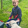child, boy, smiling, sheep, bucket, grass, outdoor, fence, animal, feeding, nature, greenery, happy, young, curly_wool, farm, playful, casual_clothing, daytime, pet
