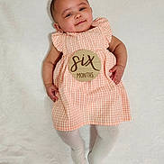 Kaylani is registered to the contest to win money with this photo: baby, infant, child, six_months, dress, orange, checkered, wooden_badge, smile, lying_down, white_background, tights, cute, portrait, soft_texture, hands, legs, head, face, happy