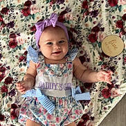 Stevie joined the competition — help win amazing prizes! baby, infant, girl, smiling, headband, bow, dress, floral_blanket, milestone_marker, five_months, floor, cute, happy, lying_down, child, indoors, soft_texture, pattern, person, portrait