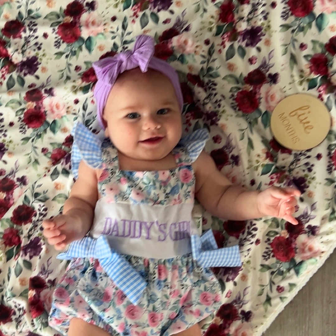 Stevie joined the competition — help win amazing prizes! baby, bow, child, cute, dress, five_months, floor, floral_blanket, girl, happy, headband, indoors, infant, lying_down, milestone_marker, pattern, person, portrait, smiling, soft_texture