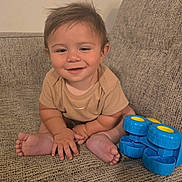 Azreal joined the competition — help win amazing prizes! baby, child, infant, smiling, sitting, couch, toy, blue_toy, wheels, indoors, portrait, happy, face, brown_hair, onesie, barefoot, playtime, furniture, home, closeup