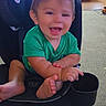 baby, child, infant, smiling, laughing, sitting, car_seat, green_shirt, barefoot, toes, indoors, living_room, home, carpet, furniture, portrait, candid, happy, face, daylight