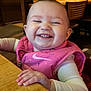 baby, child, smiling, happy, pink_vest, table, wood, indoor, restaurant, high_chair, person, face, clothing, sleeves, cute, joyful, cheerful, infant, seated, portrait