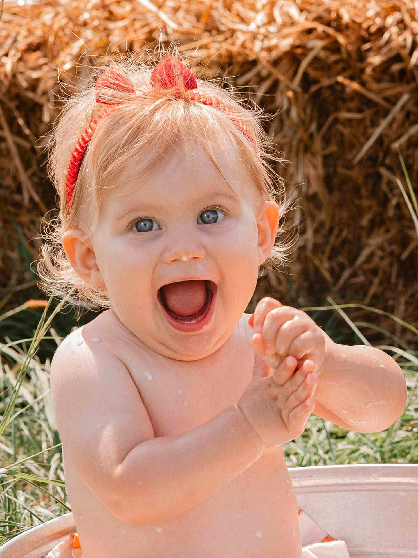Victoire participe au concours pour gagner de l'argent avec cette photo : baby, child, happy, clapping, headband, red, outdoor, grass, haystack, water_droplets, skin, smile, expression, portrait, summer, sunlight, cute, bare_shoulders, playful, person