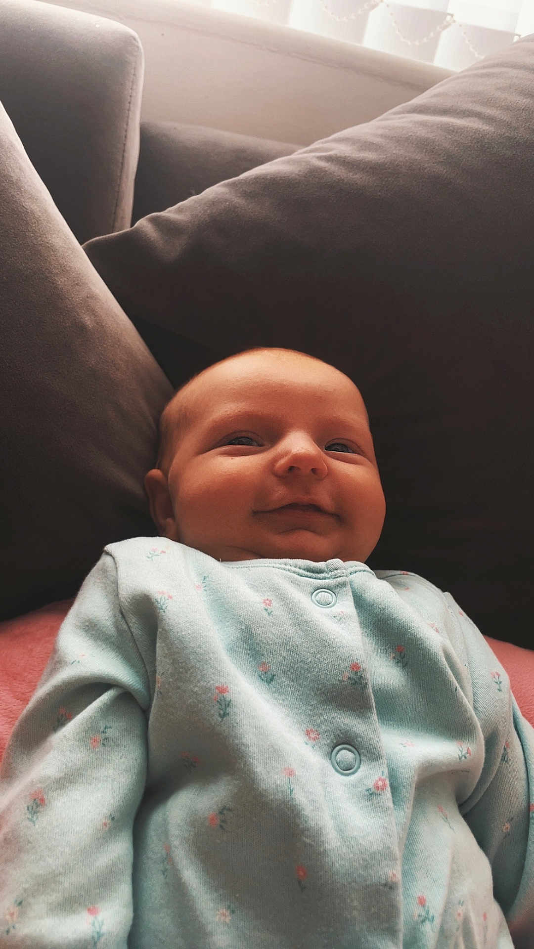 Nova-Mae is registered to the contest to win money with this photo: baby, infant, smiling, onesie, floral_print, cushion, sofa, soft_lighting, indoor, cozy, child, portrait, cute, relaxed, comfortable, happy, head, face, clothing, home