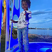 Ayden joined the competition — help win amazing prizes! child, boy, standing, blue_light, platform, waterfront, river, sky, clouds, trees, palm_tree, casual_clothing, jeans, tshirt, slippers, outdoor, evening, pose, playful, nature