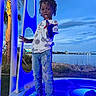 child, boy, standing, blue_light, platform, waterfront, river, sky, clouds, trees, palm_tree, casual_clothing, jeans, tshirt, slippers, outdoor, evening, pose, playful, nature