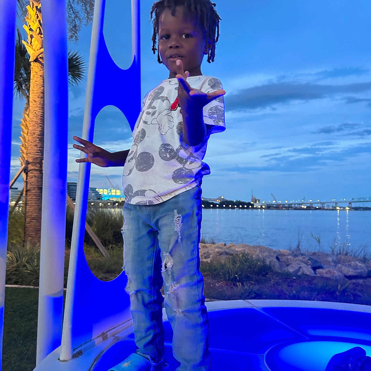 Ayden joined the competition — help win amazing prizes! child, boy, standing, blue_light, platform, waterfront, river, sky, clouds, trees, palm_tree, casual_clothing, jeans, tshirt, slippers, outdoor, evening, pose, playful, nature