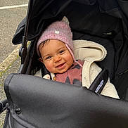 Jennah a rejoint le concours — aidez-le/la à gagner de superbes lots ! baby, child, stroller, pram, beanie, hat, smile, happy, cheeks, jacket, coat, blanket, canopy, seat_harness, infant, portrait, outdoor, pavement, walking_path, cozy