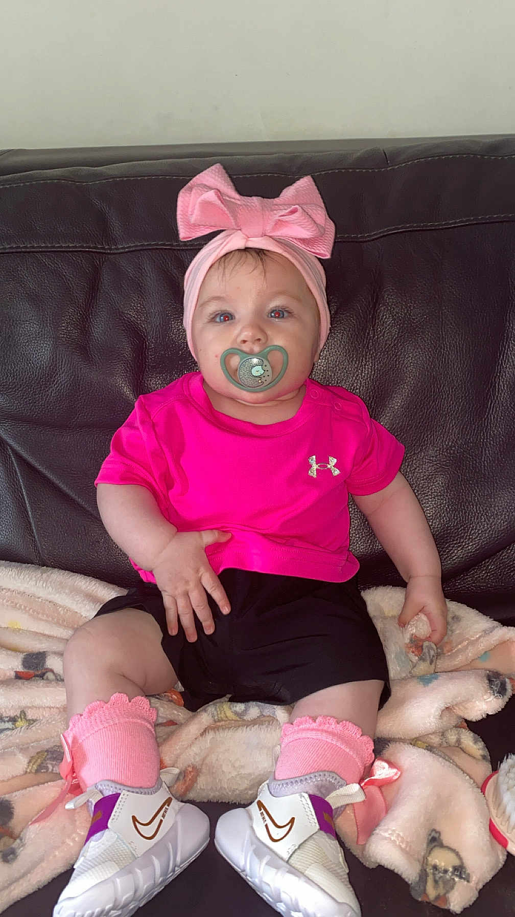 Maria a rejoint le concours — aidez-le/la à gagner de superbes lots ! baby, child, pacifier, pink_bow, pink_shirt, black_shorts, pink_socks, white_sneakers, blanket, leather_couch, indoor, infant, cute, headband, footwear, sitting, portrait, clothing, comfortable, young_child