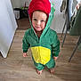 toddler, child, costume, dinosaur, hood, red, green, yellow, onesie, barefoot, indoor, wooden_floor, curious, standing, person, clothing, cute, face, expression, home