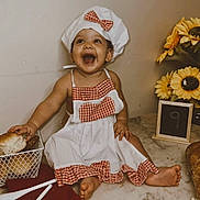 Rebecca is registered to the contest to win money with this photo: baby, child, chef_hat, apron, smiling, happy, bread, cookie, kitchen_utensils, marble_countertop, sunflowers, flower_arrangement, food, sitting, cute, infant, table, red_checkered_pattern, playful, indoor