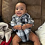 Kyngstun is registered to the contest to win money with this photo: baby, child, smiling, plaid_shirt, couch, blanket, pillow, indoor, happy, cute, infant, seated, clothing, comfortable, young_child, portrait, skin, face, hands, legs