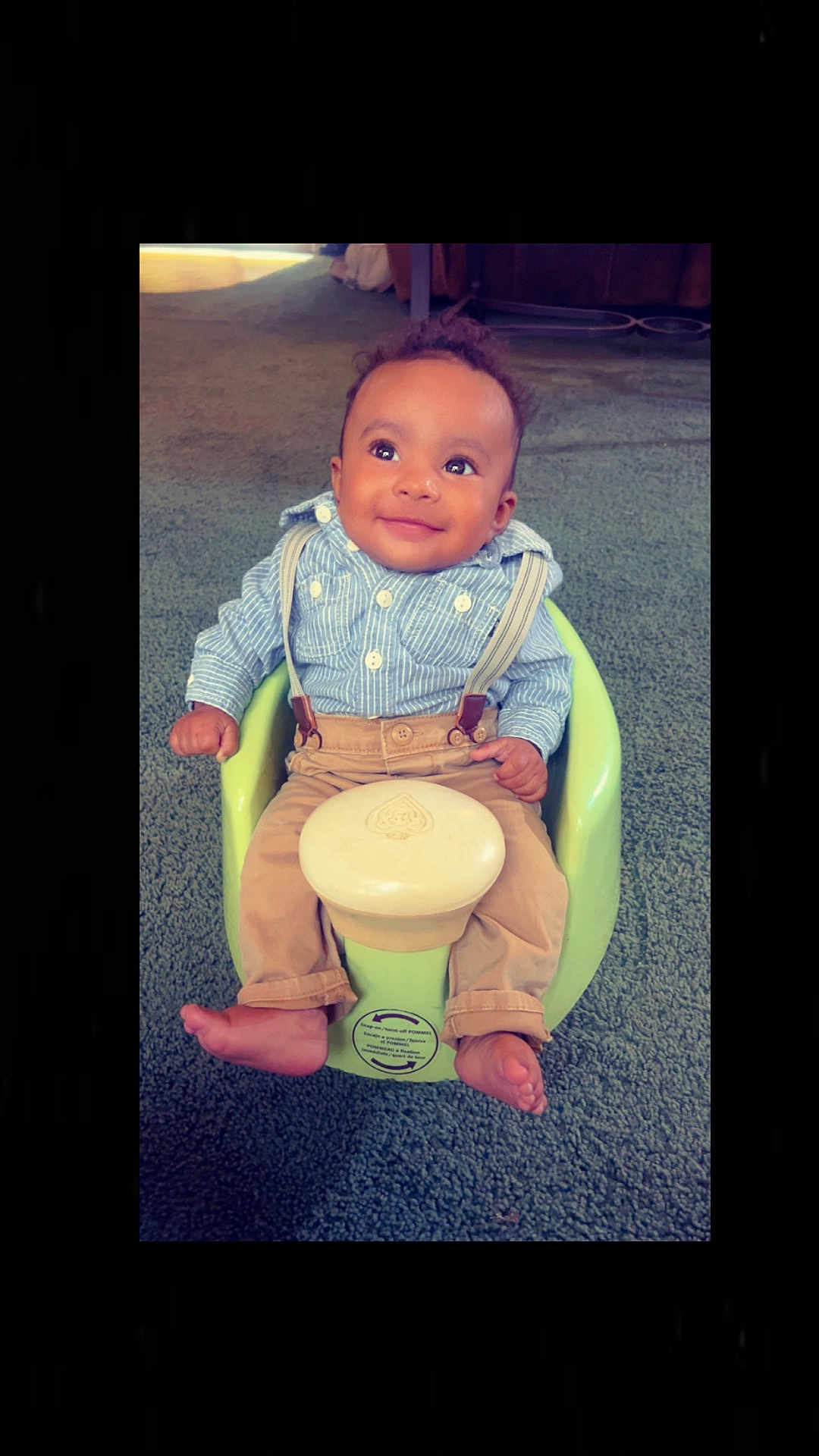 Kyngstun is registered to the contest to win money with this photo: baby, child, suspenders, blue_shirt, beige_pants, barefoot, green_baby_seat, carpet, smiling, portrait, indoor, cute, infant, small_hands, small_feet, happy, seated, looking_up, curly_hair, person