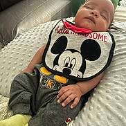 Hugo Lee is registered to the contest to win money with this photo: baby, sleeping, bib, mickey_mouse, clothing, pants, yellow_socks, cushion, plush_toy, bed, blanket, hand, infant, resting, indoors, comfort, cute, child, soft_lighting, peaceful