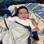 Dariel is registered to the contest to win money with this photo: baby, infant, child, portrait, smiling, face, bed, blanket, mittens, socks, clothing, lying_down, cozy, indoor, bedroom, bedding, textile, colorful, relaxed, photography