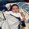 baby, infant, child, portrait, smiling, face, bed, blanket, mittens, socks, clothing, lying_down, cozy, indoor, bedroom, bedding, textile, colorful, relaxed, photography