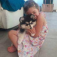 Lila a rejoint le concours — aidez-le/la à gagner de superbes lots ! child, girl, puppy, dog, hug, smile, floral_dress, indoor, floor, barefoot, cute, pet, affection, home, furniture, stacked_boxes, cozy, young, happy, playful