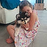 child, girl, puppy, dog, hug, smile, floral_dress, indoor, floor, barefoot, cute, pet, affection, home, furniture, stacked_boxes, cozy, young, happy, playful