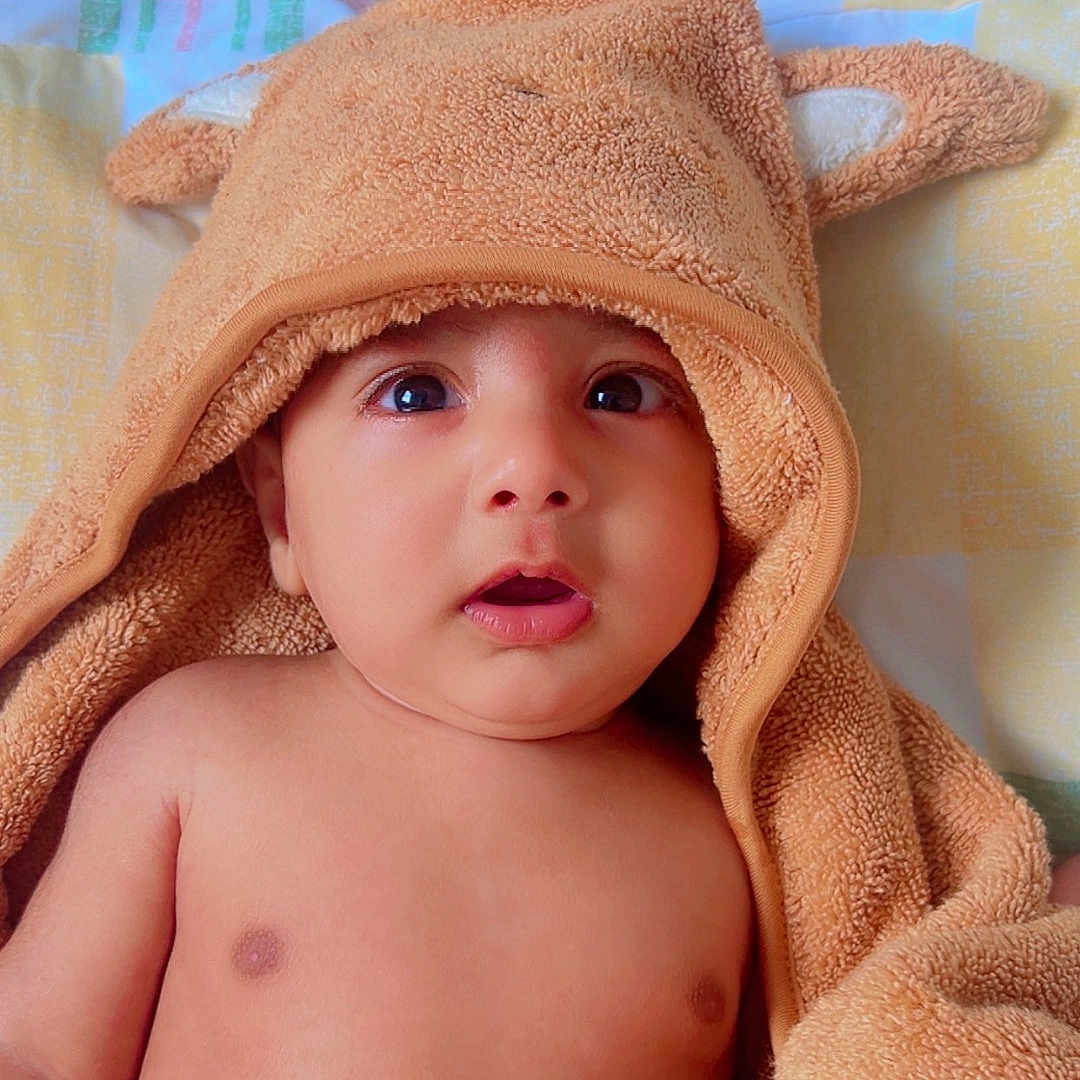 Teghbir Singh joined the competition — help win amazing prizes! baby, bed, blanket, child, closeup, curious, cute, ears, expression, hooded_towel, indoors, infant, lying_down, orange, portrait, skin, soft_texture, towel, wide_eyes, wooden_headboard