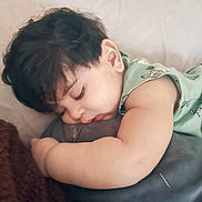 Amir is registered to the contest to win money with this photo: toddler, sleeping, child, curly_hair, plush_toy, green_clothing, blanket, resting, peaceful, indoors, soft_texture, cute, face, arm, baby, cozy, nap, person, young_child, close_up