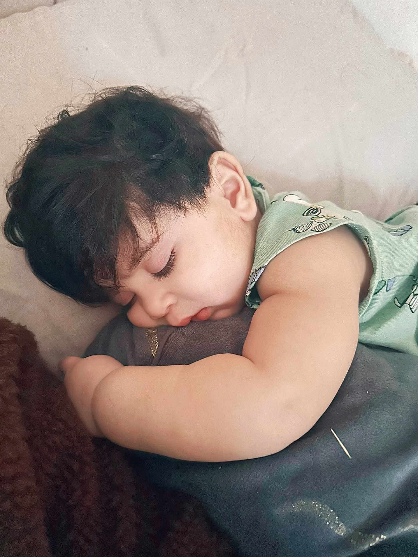 Amir is registered to the contest to win money with this photo: toddler, sleeping, child, curly_hair, plush_toy, green_clothing, blanket, resting, peaceful, indoors, soft_texture, cute, face, arm, baby, cozy, nap, person, young_child, close_up