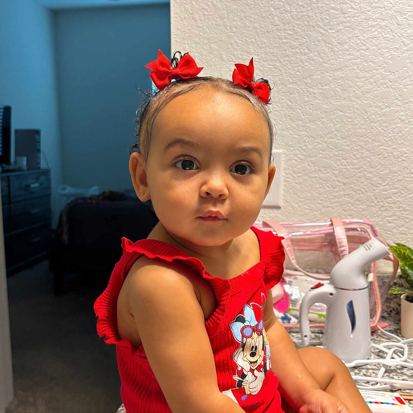 Asiya joined the competition — help win amazing prizes! toddler, child, red_clothing, hair_bows, sitting, indoor, kitchen_counter, cotton_swab, curious_expression, household_items, steamer, wall_outlet, plant, granite_countertop, person, portrait, baby, cute, face, small_child