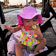 Asiya is registered to the contest to win money with this photo: baby, child, pink_hat, swimsuit, teething_toy, stroller, pool, water_umbrella, sunset, palm_trees, outdoor, towel, beads, smiling, happy, summer, cute, infant, toy, relaxing