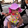 baby, child, pink_hat, swimsuit, teething_toy, stroller, pool, water_umbrella, sunset, palm_trees, outdoor, towel, beads, smiling, happy, summer, cute, infant, toy, relaxing