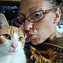 Wee G is registered to the contest to win money with this photo: woman, cat, glasses, close_up, selfie, orange_cat, white_cat, face, puckered_lips, sunflower, shirt, indoor, television, people_on_tv, affection, pet, animal, casual, hair, ear