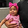 Sanaa joined the competition — help win amazing prizes! baby, child, pink_bow, onesie, cherry_pattern, smile, indoor, hand, nail_polish, person, holding, face, cute, infant, living_room, furniture, television, window_blind, black_clothing, skin